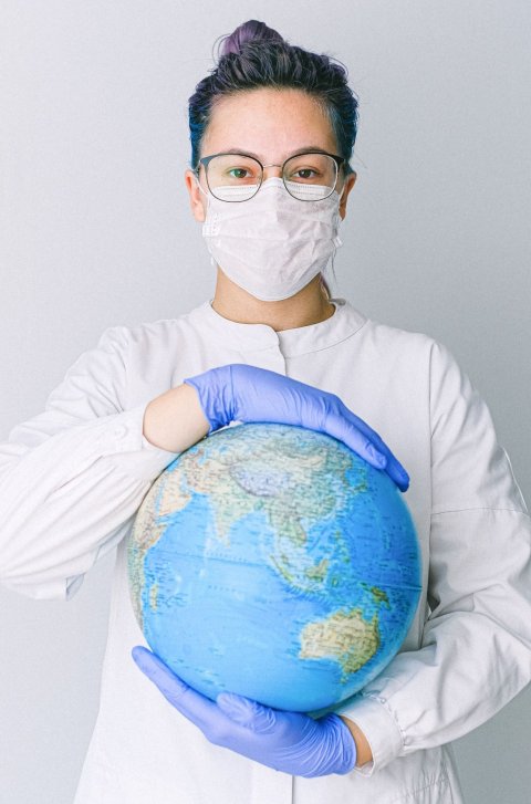 woman in white coat wearing face mask holding a globe